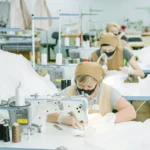 Para pekerja perempuan mengoperasikan mesin jahit industri di pabrik konveksi tekstil